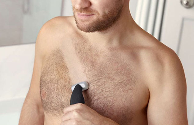 : Close-up of a man&rsquo;s hairy chest with stripe being shaven across by an electric shaver he is holding.