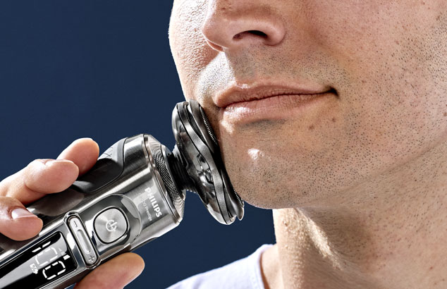 Close-up of a man&rsquo;s chin with very short stubble pressing an electric razor against his jaw.